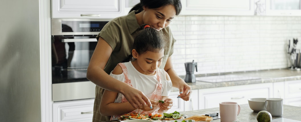 Mãe e filha praticando a alimentação consciente por cozinhar sua própria refeição e utilizar alimentos saudáveis e nutritivos. 